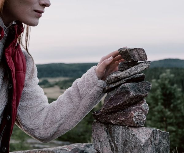 Person meditating peacefully with a balanced stone stack nearby.