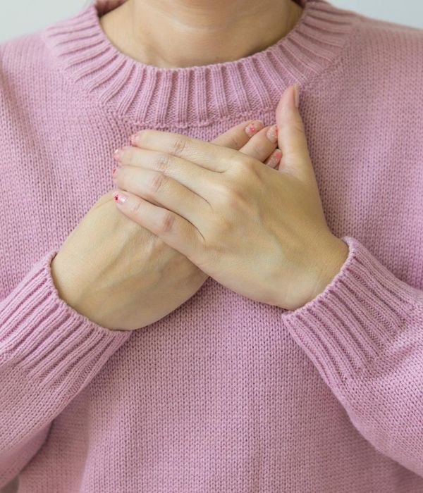 Woman in a calm yoga pose in a dark room with soft pink light.